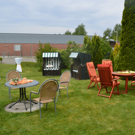 Garten mit mehreren Sitzgruppen, darunter ein runder Tisch mit Stühlen und zwei Gartenhäuschen im Hintergrund.