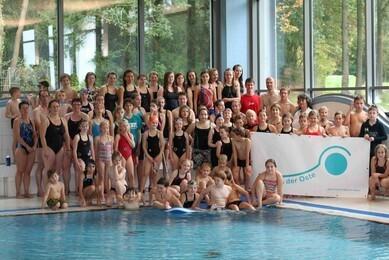 Gruppenfoto von Schwimmern unterschiedlicher Altersgruppen vor einer Schwimmhalle mit Banner &bdquo;Schwimmen an der Oste&ldquo;.