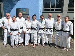 Gruppe von zehn Personen in weißen Judoanzügen mit schwarzen Gürteln vor einem Gebäude.