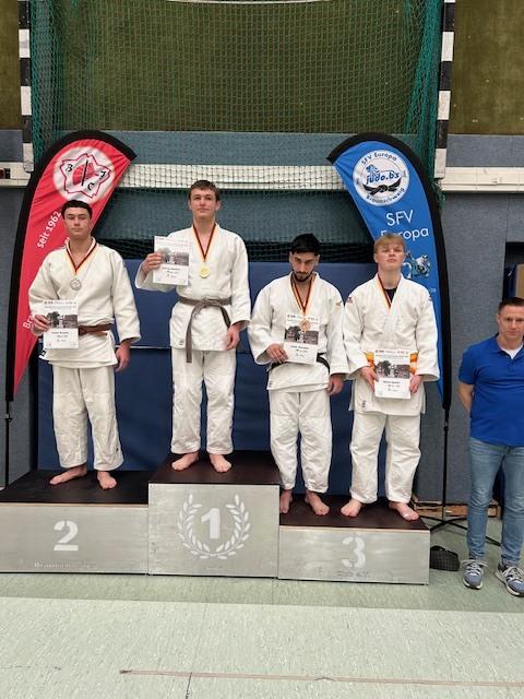 Vier Judokämpfer stehen auf dem Siegertreppchen, alle in Judokleidung, mit Medaillen und Urkunden.